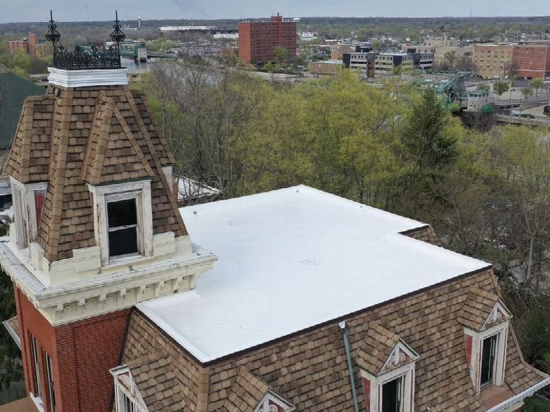 Aerial view of a new white single-ply flat roof fitted between the mansard slopes of a historic brick building