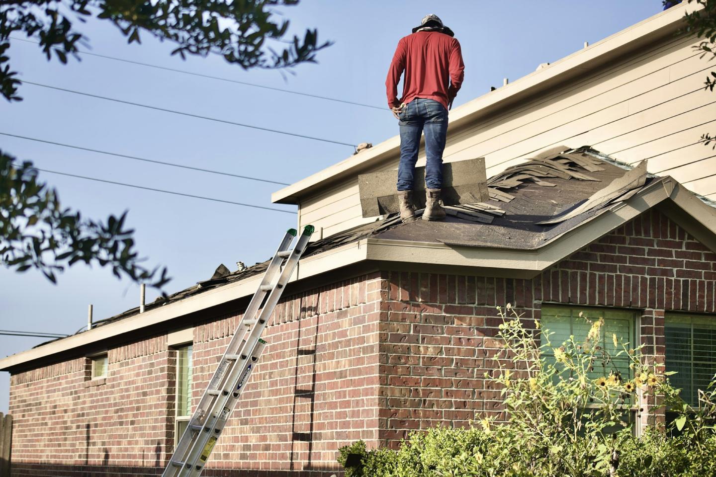An Apex Construction roofer tearing off old shingles during a residential roof replacement